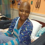 Woman with bald head sits on a hospital bed, smiling.