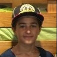 Teenager wearing a baseball cap with a logo, smiling slightly. Dark hair, blue shirt. Wood background.