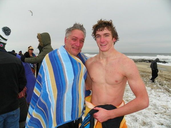 Man and young man wrapped in towels on a snowy beach after a polar bear plunge.