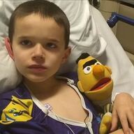 Boy in hospital bed with Bert puppet, wearing blue pajamas, looking concerned.