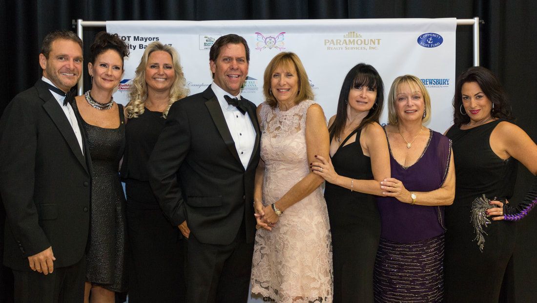 Group of people at an event pose together in front of a banner. Formal attire. Smiles.