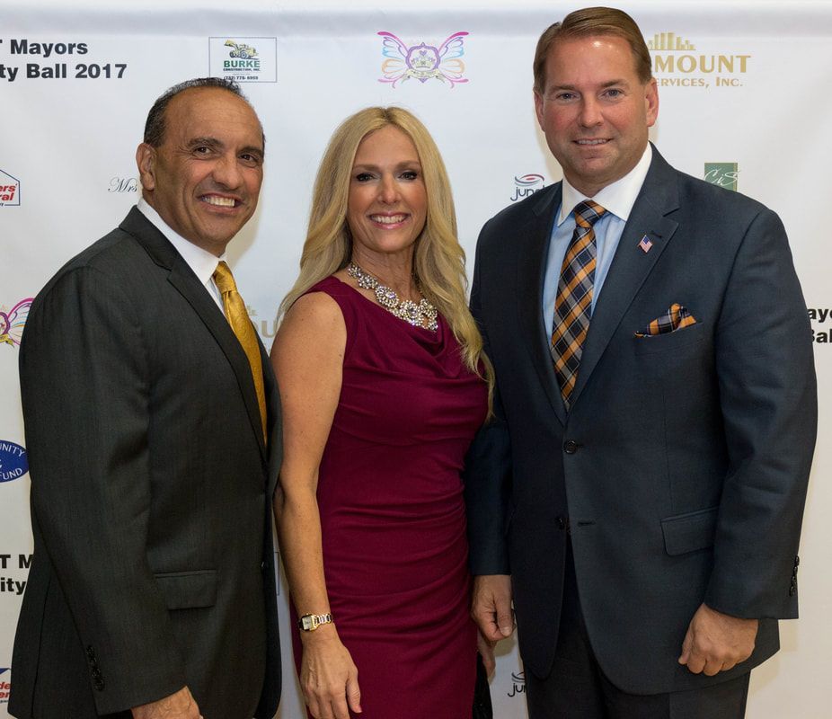 Three people at a gala event posing for a photo. Woman in a red dress with two men in suits, smiling.