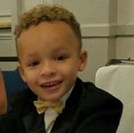 Smiling child in a tuxedo with a gold bow tie, light skin and curly hair.