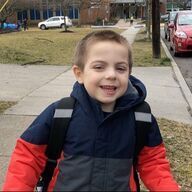 Smiling child in a winter coat and backpack, standing outside a building.