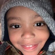 Child smiling widely, wearing a gray knitted hat with earflaps.