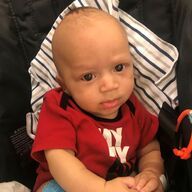 Baby in a red shirt in a striped carrier, looking at the camera.