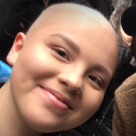 Person with shaved head smiling, looking towards the camera.