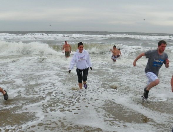 People running from ocean waves, some partially submerged, cloudy day.