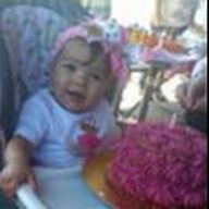 Baby in high chair with a pink cake and bow.