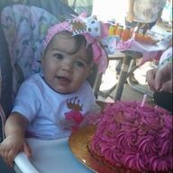 Baby with pink headband and cake at outdoor party.