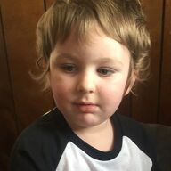 Young child with light brown hair, wearing a black and white shirt, looking down, set against a wooden background.