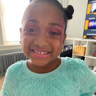 Smiling child with pink eye makeup and a light blue sweater.