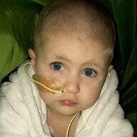 Child with blue eyes and feeding tube, wrapped in a white towel, looking at the camera.