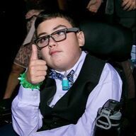 Young person in a wheelchair gives a thumbs-up. They wear glasses, a vest, and a bowtie.