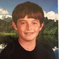 Boy with braces smiling, against a landscape of water and mountains.