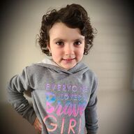 Girl with curly brown hair wearing a gray hoodie that says, 
