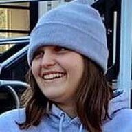 Person wearing a light blue beanie and hoodie, smiling broadly. Outdoors setting.