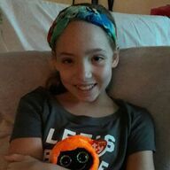 Girl with dark hair and headband holding orange stuffed animal, smiling.