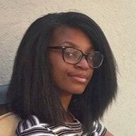 Person with glasses smiles, looking to the side. Wearing a striped shirt.