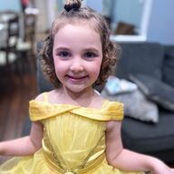 Girl in yellow Belle dress smiles, hair up in a bun.