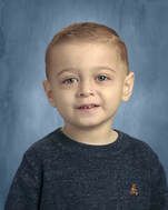 A young child with light skin smiling, wearing a blue sweater, against a blue background.