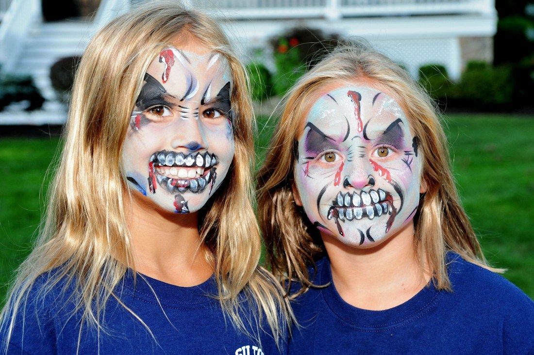 Two girls with zombie face paint, smiling, outside.