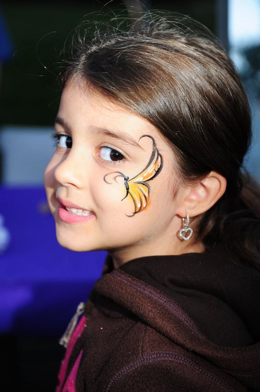 Girl with a butterfly face paint, smiling, brown hair, wearing a brown hoodie.