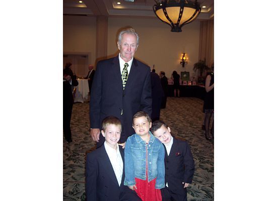 Man in suit stands with three boys in formal attire, indoors.