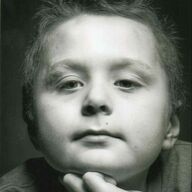 Close-up portrait of a child with light skin. Child rests chin on hand, looking at the viewer. Black and white.