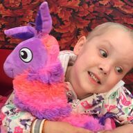 Child with a stuffed llama, making a funny face, red floral background.