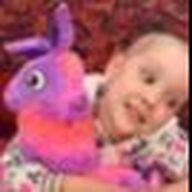 Child smiling, holding a purple and orange llama plush toy.