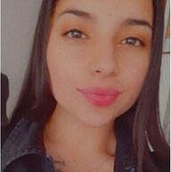 Woman with long dark hair smiles, wearing a dark jacket. Pink lipstick.