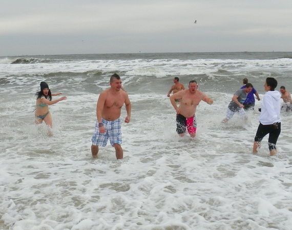People run into ocean waves on a cloudy day.
