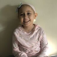 Young person with a shaved head smiles, wearing a pink headband and sweatshirt.