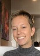 Person smiling, wearing a gray turtleneck sweater, short brown hair, indoor setting.