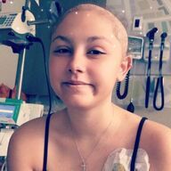 Person with a shaved head smiles, wearing a tank top, in a hospital room.