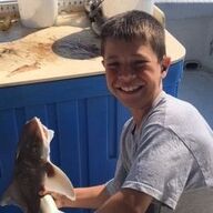 Boy smiles, holding a small fish on a boat.
