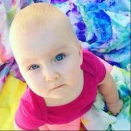 Baby with fair skin and blue eyes in a pink shirt, looking upwards, on a colorful tie-dye blanket.