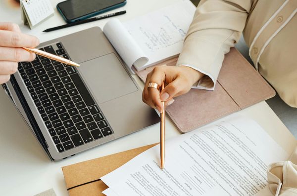 A person is writing on a piece of paper in front of a laptop computer.