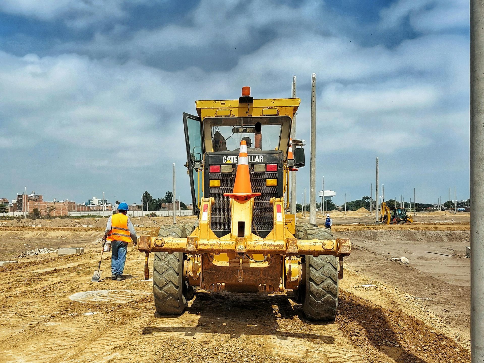A man is standing next to a yellow caterpillar tractor on a dirt road.