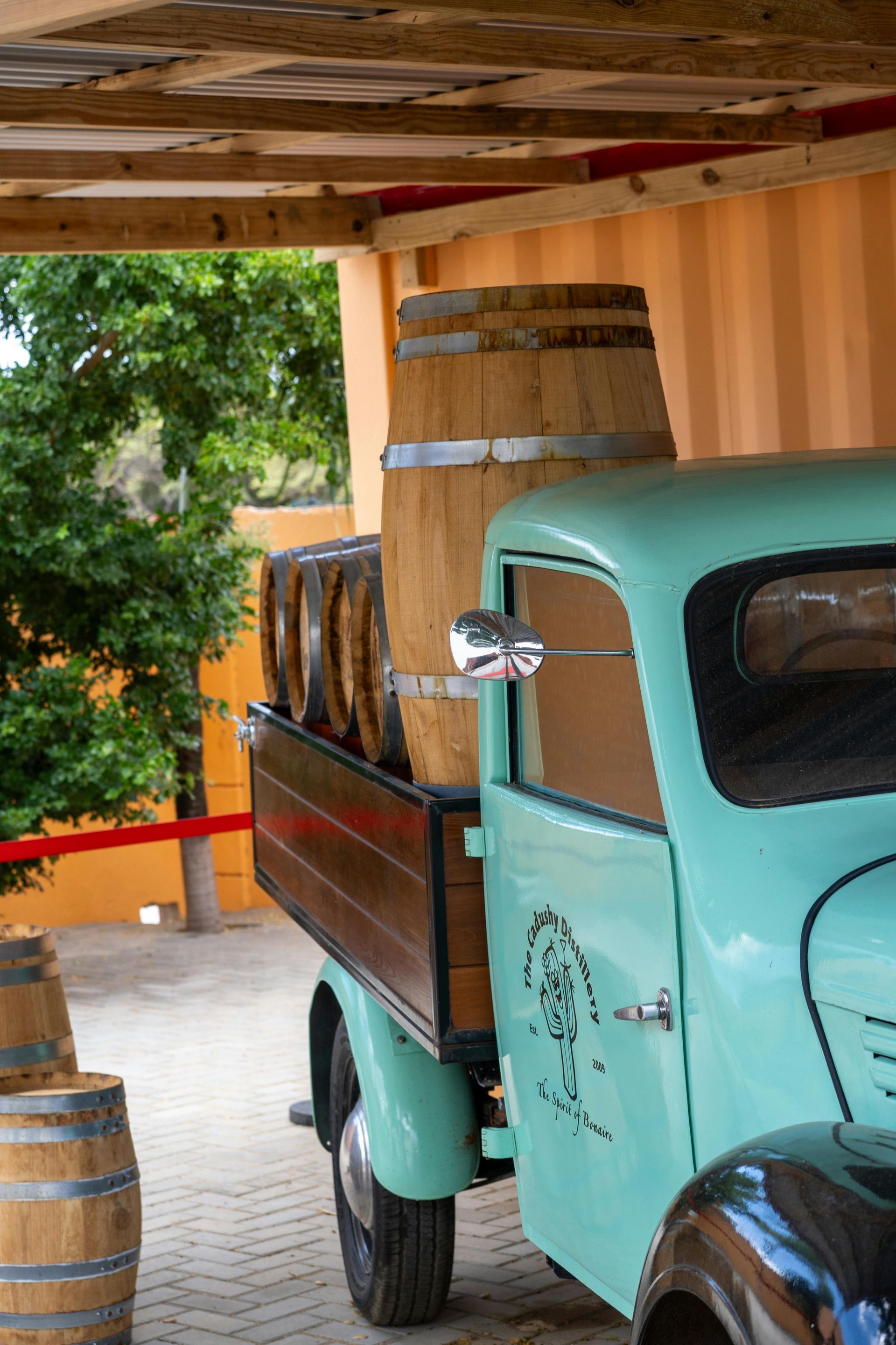 Teal vintage truck with wooden bed, carrying wine barrels. Under a wooden awning.