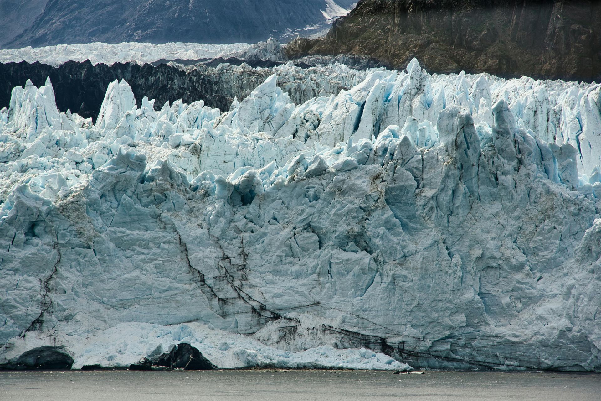Ice glacier with jagged peaks and blue crevices against a dark mountain backdrop.