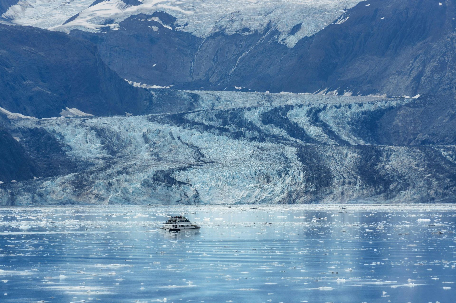 Boat on water in front of a glacier with a mountainous background.