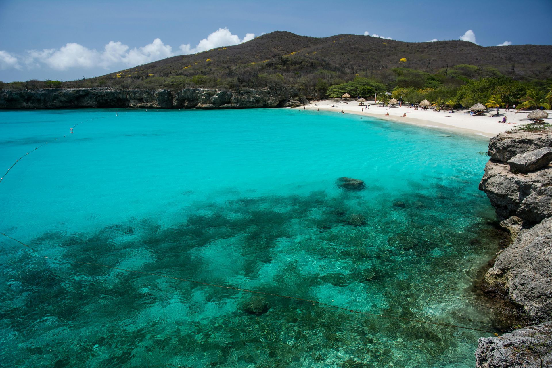 Turquoise ocean meets white sand beach under a mountain. Rocky cliffs frame the view.