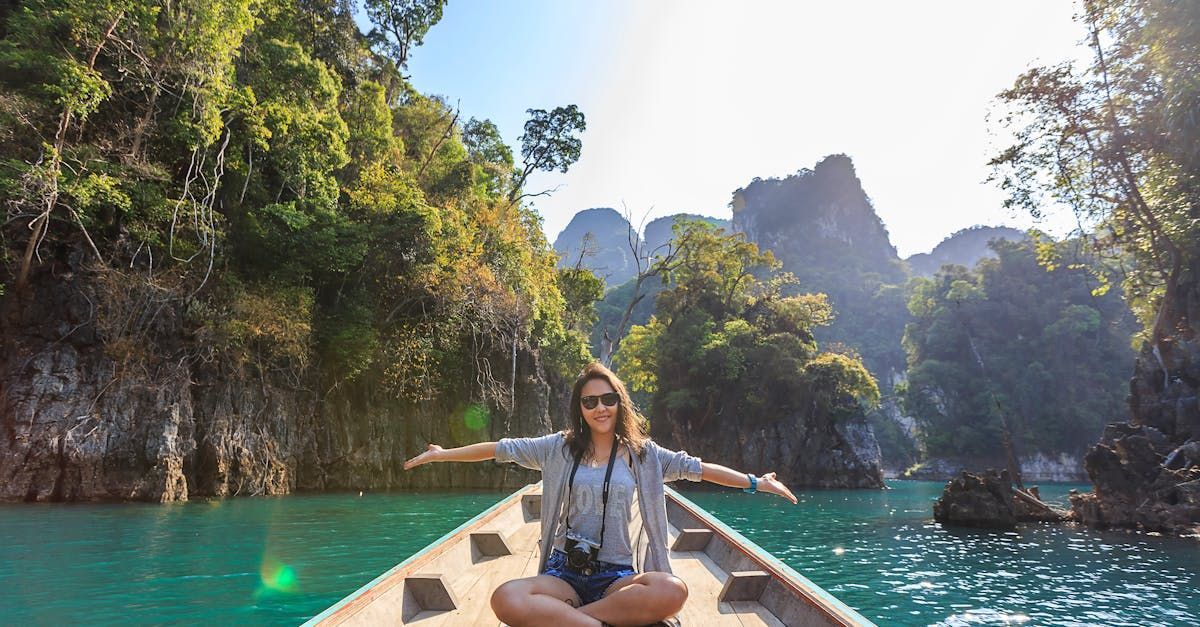 Woman on boat with arms outstretched, surrounded by turquoise water and lush green islands.