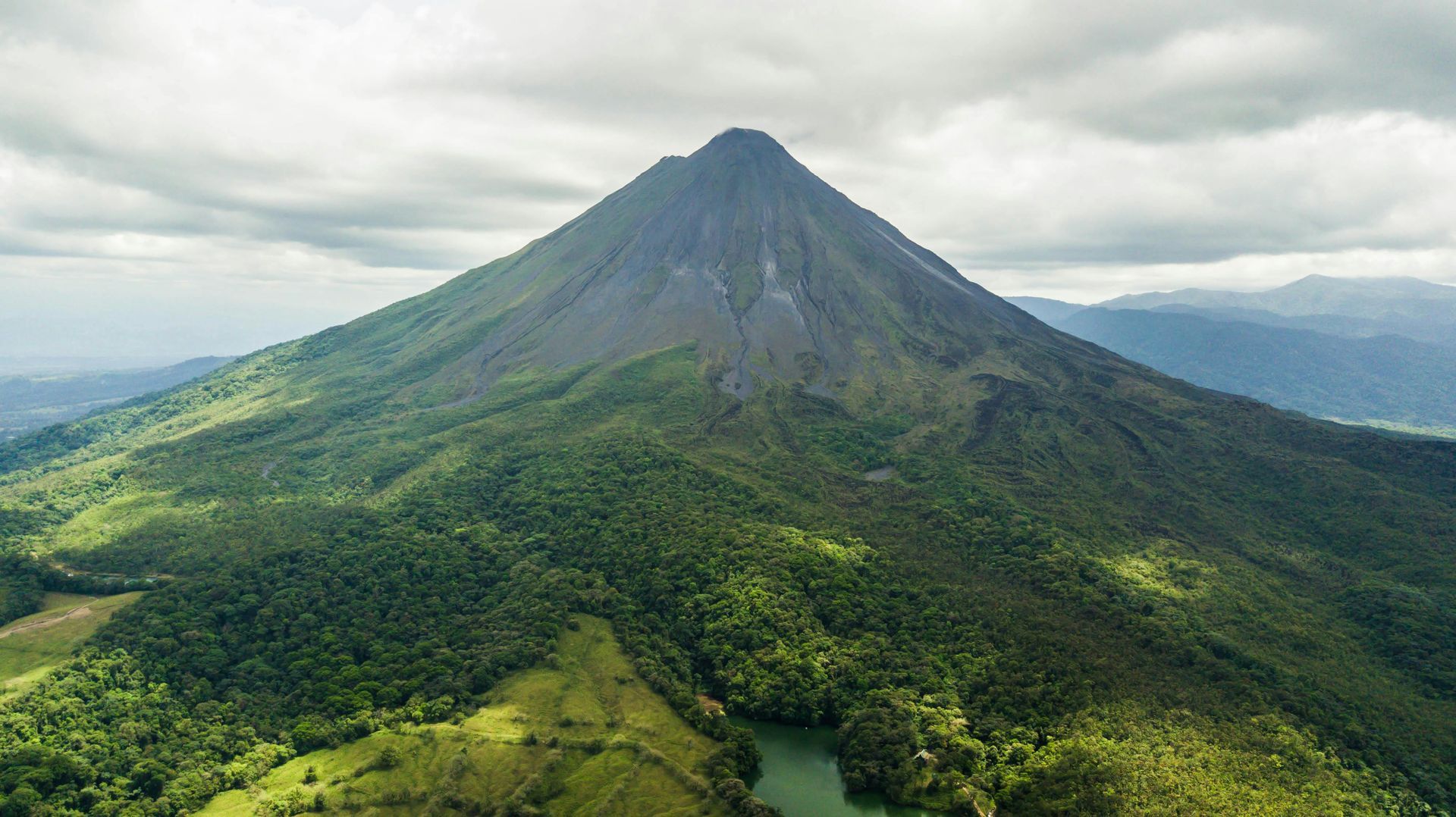 A lush green volcano with a dark, rocky peak under a cloudy sky.