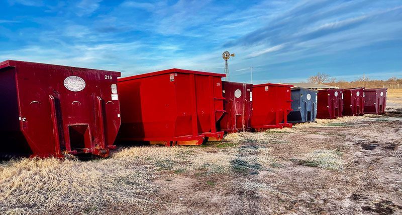 a row of red dumpsters are lined up in a dirt field .