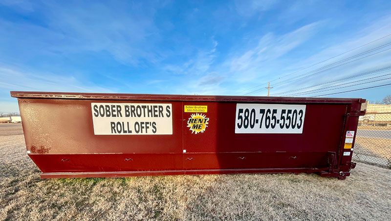 a large red dumpster is sitting on top of a dirt field .