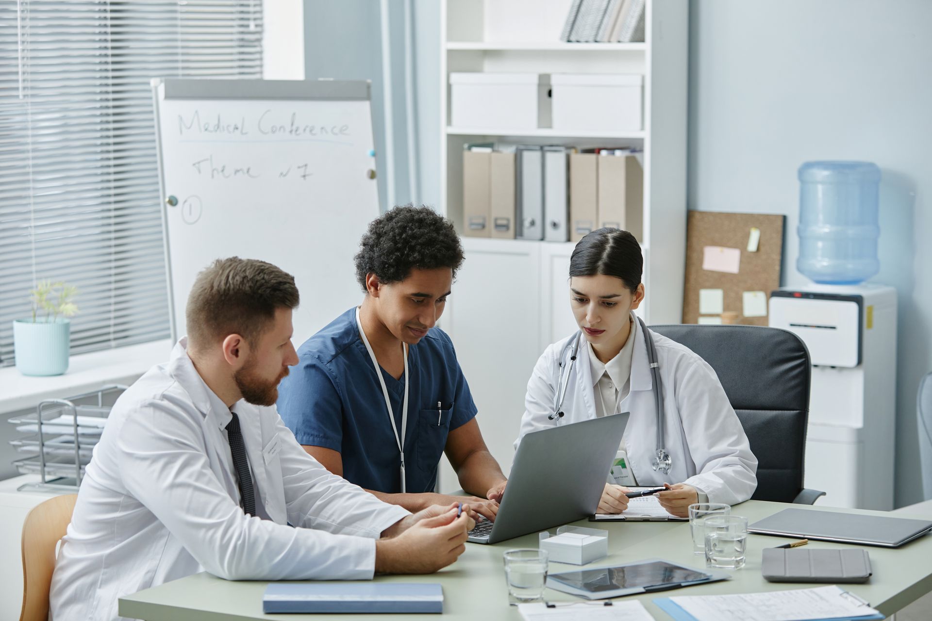 A group of doctors and nurses are sitting around a table looking at a laptop.