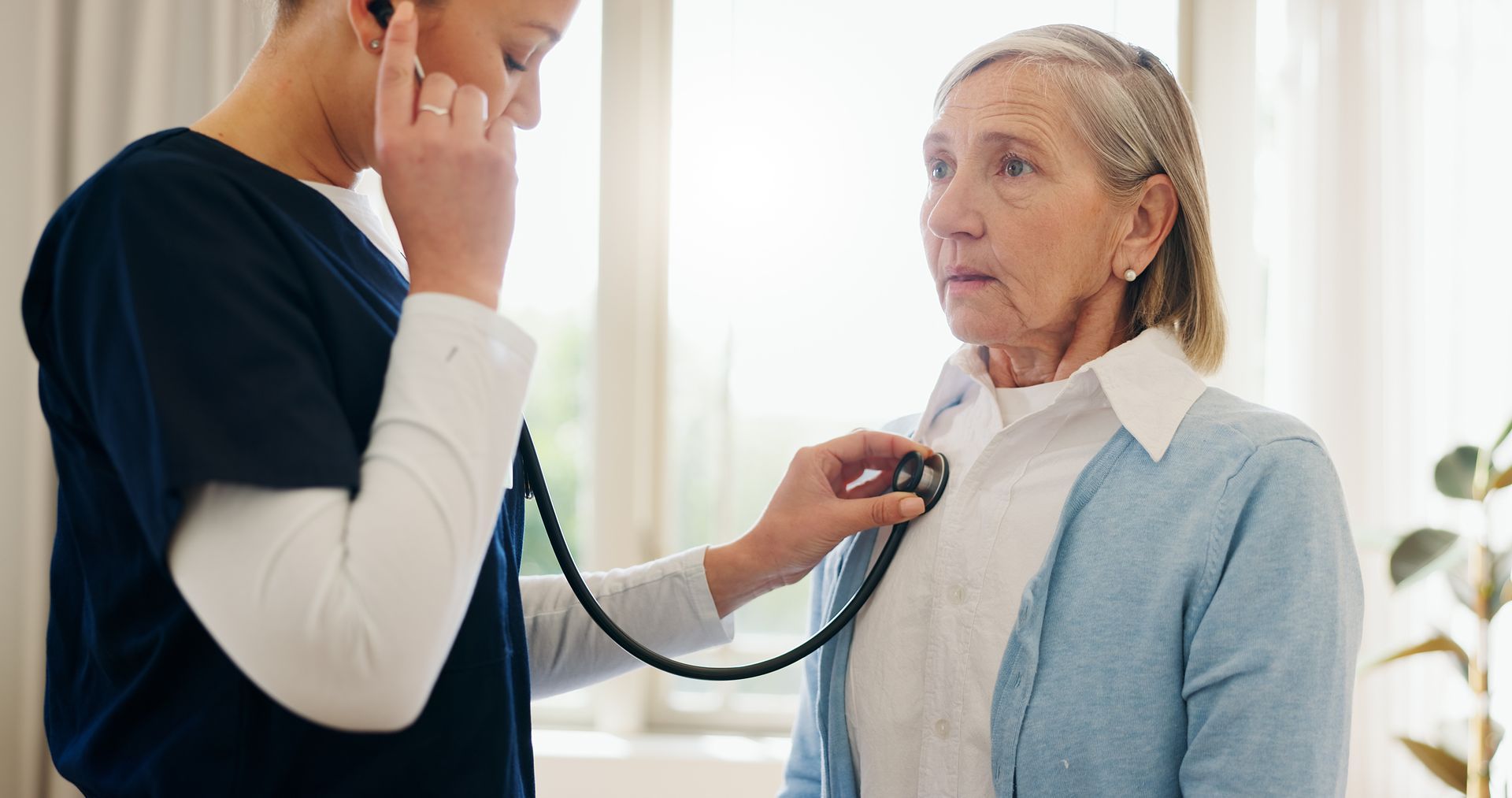 A nurse is listening to an elderly woman 's heart with a stethoscope.